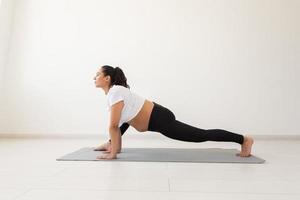 Young flexible pregnant woman doing gymnastics on rug on the floor on white background. The concept of preparing the body for easy childbirth photo