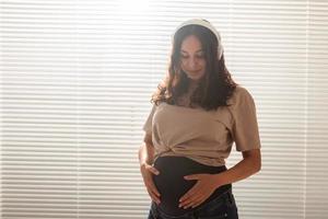 Happy pregnant woman with curly hair listening music in headphones, copy space. photo