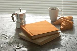 naturaleza muerta para una agradable taza de café matutino y croissants con dos libros sobre la mesa. concepto de descanso para almorzar o comenzar la mañana foto