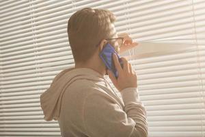 Pensive guy is talking on his smartphone and looking at window at home. Male thinking dreaming and looking out the window. photo