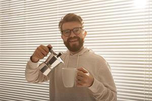 Young man pouring coffee from moka pot at morning. Breakfast and break concept. photo