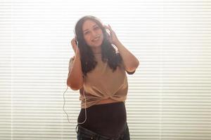 Happy pregnant woman with curly hair listening music in headphones with copy space. photo