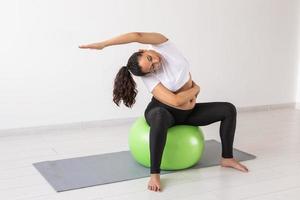 Young flexible pregnant woman doing gymnastics on rug on the floor on white background. The concept of preparing the body for easy childbirth photo