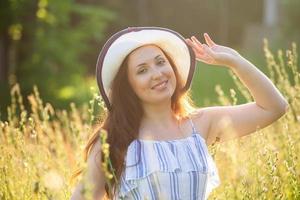 Happy young woman with long hair in hat and dress walking through the summer forest on a sunny day. Summer joy concept photo