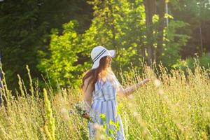 mujer joven caminando entre flores silvestres en un día soleado de verano. concepto de la alegría de comunicarse con la naturaleza de verano foto