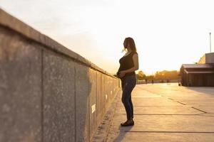Pregnant hispanic woman on embankment, touching belly. Copy space. photo
