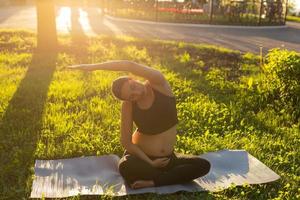 Pregnant woman doing yoga in nature outdoors. Healthy lifestyle, expecting baby and childbearing concept. photo