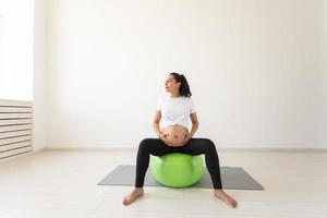 A young pregnant woman doing relaxation exercise using a fitness ball while sitting on a mat. photo