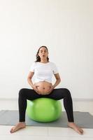 beautiful young pregnant woman doing exercise at home on fitball photo