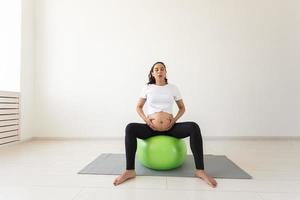 A young pregnant woman doing relaxation exercise using a fitness ball while sitting on a mat. Copyspace. photo