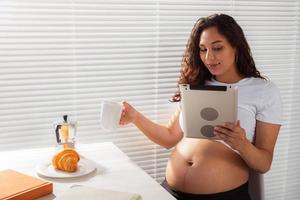 mujer embarazada usando tableta digital. hora del desayuno. tecnología y concepto de embarazo. foto