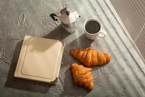 naturaleza muerta para una agradable taza de café por la mañana y croissants con un libro sobre la mesa. concepto de descanso para almorzar o comenzar la mañana foto