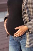 Active pregnancy concept. Close-up of belly of happy young business or student pregnant woman standing in a park. Future mom working or studying on her late pregnancy period. photo