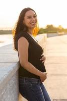 Portrait of hispanic pregnant woman walking on embankment at sunset. Pregnancy and motherhood concept. photo