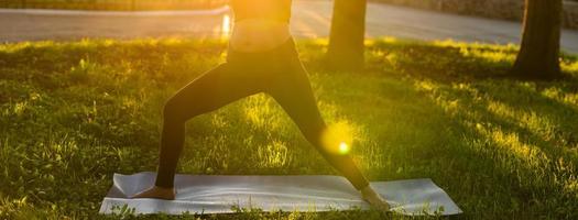 Banner pregnant woman belly in black tracksuit makes heroe pose standing barefoot on rug on green lawn on sunny summer day copy space. Childbirth preparation and nervous calming concept photo