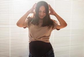 Smiling brunette pacified pregnant woman listening to pleasant music using a smartphone and headphones. Sedation therapy concept before meeting with baby photo