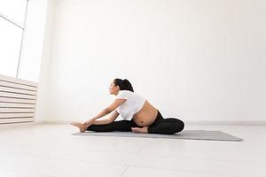 una mujer embarazada decidida hace ejercicio durante la clase de yoga y se relaja mientras se sienta en una alfombra en el suelo. concepto de preparación física y mental del cuerpo para el parto. lugar para texto foto