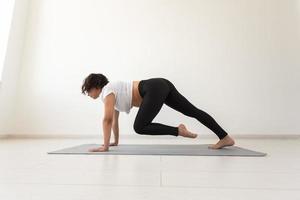 joven mujer embarazada flexible haciendo gimnasia sobre una alfombra en el suelo sobre fondo blanco. el concepto de preparar el cuerpo para un parto fácil foto