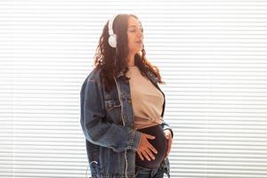 Beautiful young peaceful pregnant woman listens to pleasant classical music using smartphone and headphones. Concept of positive attitude before childbirth photo