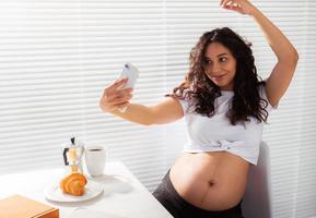 mujer embarazada tomando un autorretrato con su teléfono inteligente mientras desayuna foto