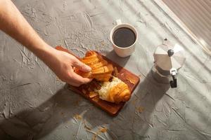 desayuno con croissant en tabla de cortar y café negro. concepto de comida y desayuno por la mañana. foto