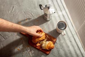 Breakfast with croissant on cutting board and black coffee. Morning meal and breakfast concept. photo