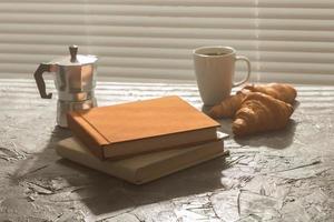 naturaleza muerta para una agradable taza de café matutino y croissants con dos libros sobre la mesa. concepto de descanso para almorzar o comenzar la mañana foto