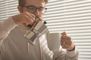 Close-up portrait of young stylish hipster male pouring coffee at office on summer day. Concept of invigorating morning and positive mood photo