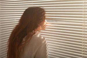 la vista trasera de una hermosa joven con el pelo largo se asoma por un agujero en las persianas de la ventana y mira por la ventana. concepto de vigilancia y curiosidad foto