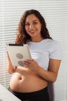 mujer embarazada usando tableta digital. hora del desayuno. tecnología y concepto de embarazo. foto