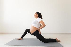 una mujer embarazada decidida hace ejercicio durante la clase de yoga y se relaja mientras se sienta en una alfombra en el suelo. concepto de preparación física y mental del cuerpo para el parto. lugar para texto foto