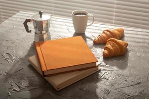 naturaleza muerta para una agradable taza de café matutino y croissants con dos libros sobre la mesa. concepto de descanso para almorzar o comenzar la mañana foto