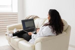 Latin pregnant woman using laptop sitting on sofa at home. Pregnancy and information for parenthood concept. photo