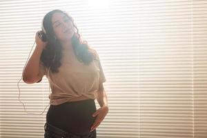 Pregnant woman listen to music in headphones at home and dances, copy space. photo