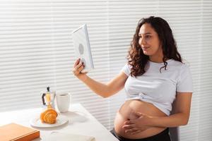 mujer embarazada usando tableta digital. hora del desayuno. tecnología y concepto de embarazo. foto