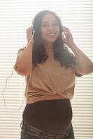 Curly-haired brunette pacified pregnant woman listens to music using smartphone and headphones. Concept of a soothing mood before meeting baby. photo