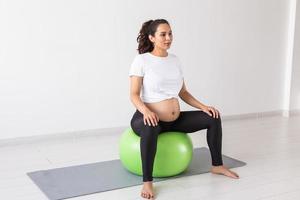 A young pregnant woman doing relaxation exercise using a fitness ball while sitting on a mat. Copyspace photo