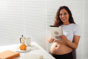 mujer embarazada usando tableta digital. hora del desayuno. tecnología y concepto de embarazo. foto