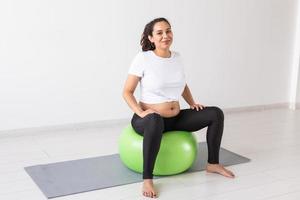 beautiful young pregnant woman doing exercise at home on fitball photo