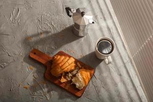 Breakfast with croissant on cutting board and black coffee. Morning meal and breakfast concept. Top view. photo