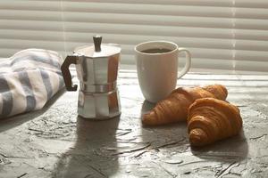 Breakfast with croissant on cutting board and black coffee. Morning meal and breakfast concept. photo