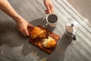 desayuno con croissant en tabla de cortar y café negro. concepto de comida y desayuno por la mañana. foto