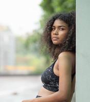 Young woman standing, confident looking, portrait. A beautiful African American person has attractive curly afro hair. Modern multi-ethnic girl enjoy carefree relaxing outside with cool posing photo