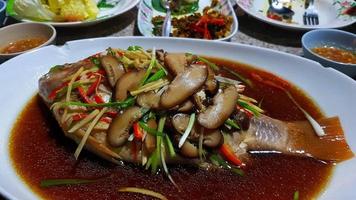 Close up Steamed Sea Bass with Soy Sauce and fresh vegetable, sliced mushrooms, ginger, red chili and spring onion on white plate or dish in Chianese style. photo