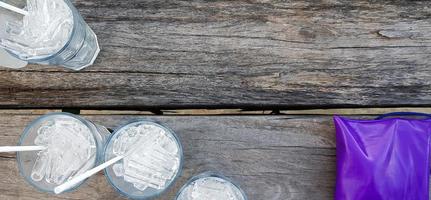 Top view of glass of ice with purple or violet leather bag on gray wooden background with copy space. Flat lay Group of drinking on wood panel wallpaper. photo