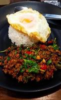 Close up spicy stir fried minced beef with basil and fried egg on white rice in Thai style on black dish or plate at local restaurant. Famous or Asian food in Thailand. photo