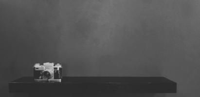 cámara vintage o de película colocada en un estante negro con fondo de pared gris oscuro y espacio de copia en estilo monocromo. objeto retro o antiguo sobre papel pintado de hormigón gris en tono blanco y negro. foto