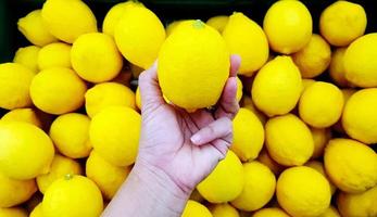 Close up hand of person holding lemon with copy space. Selection and Choice for buy best food, vegetable or fruit at market or supermarket. photo