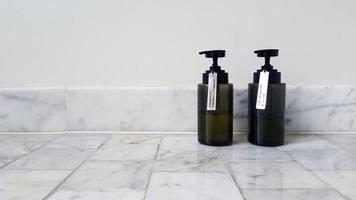 Two black plastic conditioner shampoo and bath shower gel putting on marble floor with white cement wall background with copy space on right. Cleaning part of body and Spa concept