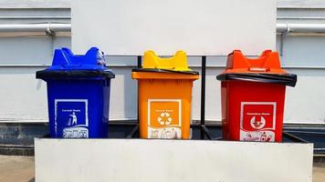 Colorful three bins for separate trash for reuse and disposal at park. Trashcan for dumping used stuff or material with white gas or oil pipeline background . photo